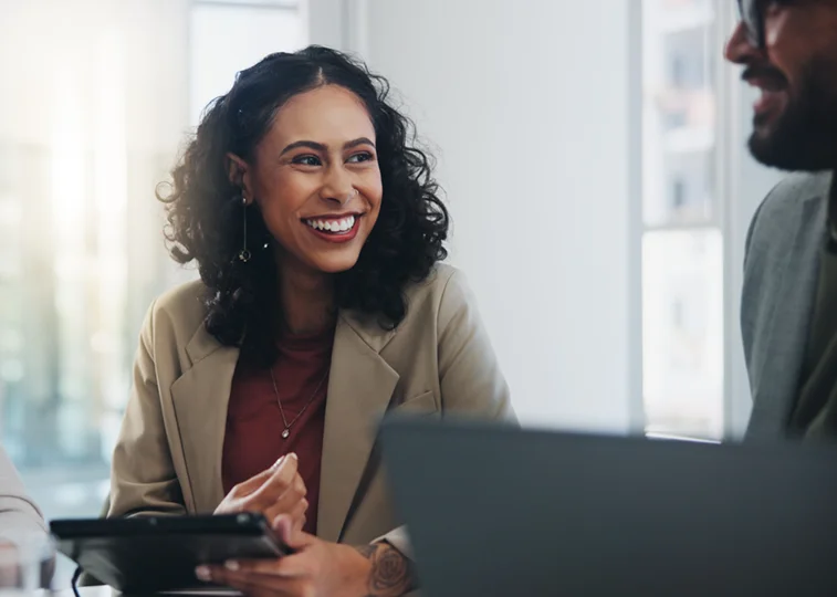 A confident woman holes a tablet while chatting with a colleague